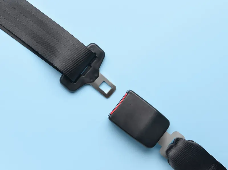 A seatbelt latch plate on webbing and a separate buckle section laid apart on a plain pale blue surface.